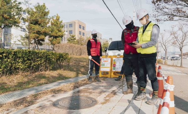 SK텔레콤과 SK오앤에스 작업자들이 IoT 센서로 측정한 맨홀 내부 정보를 스마트폰으로 확인하고 작업을 진행하고 있다.